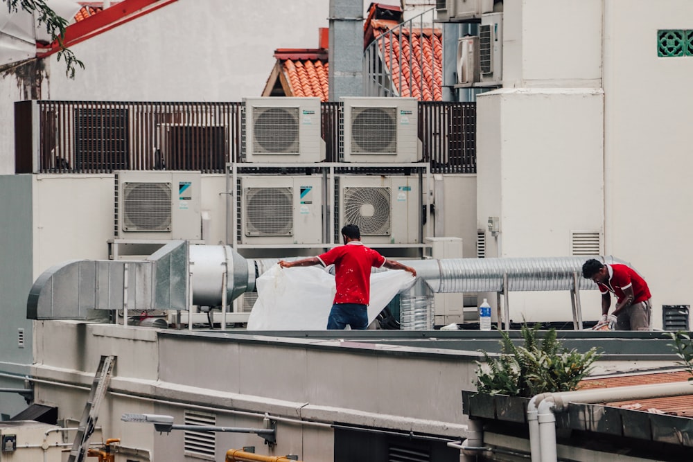 Two men in red shirts standing on a roof and inspecting HVAC systems 