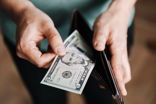 A person placing back a five-dollar bill in the wallet